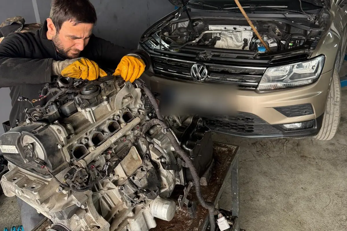 Sökülmüş motor üzerinde çalışan servis teknisyeni, arkada kaputu açık Volkswagen Tiguan