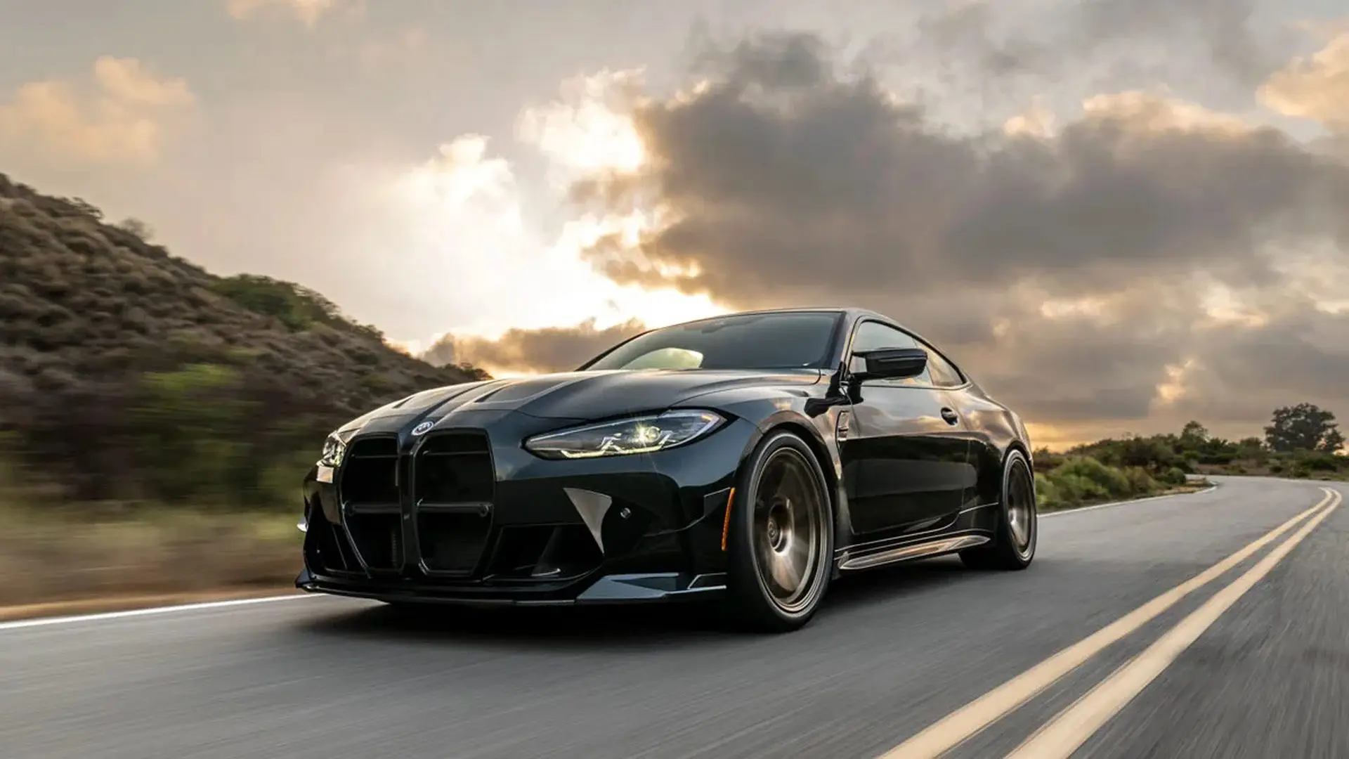 Gün batımında virajlı yolda ilerleyen siyah BMW M4 coupé